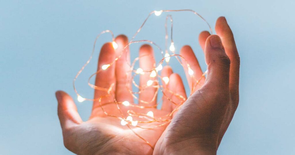 duas mãos seguram um fio com luzes contra um fundo azul, numa representação do que é segurar novas ideias e antecipar o que podem vir a ser